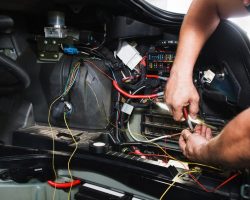 Electrician works with electric block in car. Close-up of automobile inside under raised hood. Service man hands working with cables of auto